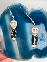 Load image into Gallery viewer, This set of earrings features a mini howlite skull bead with a wood carved black and white bead. Perfect for any goth, emo, witchy, or Day of the Dead outfit, it adds a unique touch to any ensemble.  Measurements: 1 1/2 ” in length 
