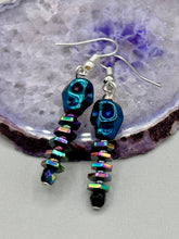 Load image into Gallery viewer, Spooky blue skull beads come with rainbow hematite spine earrings. These stylish skull earrings are perfect for adding a unique flair to any outfit. Whether you&#39;re looking for a Dia De Los Muertos accessory or simply looking to draw inspiration, these goth pieces perfectly capture the vampire goth, witchy, dark, Chingona Cabrona, Latina Chicana styles.   Measurements: 1 1/4” in length
