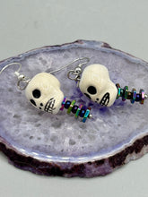 Load image into Gallery viewer, Peruvian off white ceramic skull beads come with rainbow hematite spine earrings. These stylish skull earrings are perfect for adding a unique flair to any outfit. Whether you&#39;re looking for a Dia De Los Muertos accessory or simply looking to draw inspiration, these goth pieces perfectly capture the vampire goth, witchy, dark, Chingona Cabrona, Latina Chicana styles.  Measurements: 1 1/4” in length
