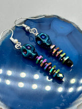 Load image into Gallery viewer, Spooky blue skull beads come with rainbow hematite spine earrings. These stylish skull earrings are perfect for adding a unique flair to any outfit. Whether you&#39;re looking for a Dia De Los Muertos accessory or simply looking to draw inspiration, these goth pieces perfectly capture the vampire goth, witchy, dark, Chingona Cabrona, Latina Chicana styles.   Measurements: 1 1/4” in length
