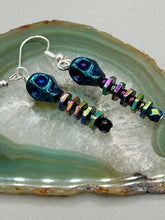 Load image into Gallery viewer, Spooky blue skull beads come with rainbow hematite spine earrings. These stylish skull earrings are perfect for adding a unique flair to any outfit. Whether you&#39;re looking for a Dia De Los Muertos accessory or simply looking to draw inspiration, these goth pieces perfectly capture the vampire goth, witchy, dark, Chingona Cabrona, Latina Chicana styles.   Measurements: 1 1/4” in length
