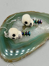 Load image into Gallery viewer, Peruvian off white ceramic skull beads come with rainbow hematite spine earrings. These stylish skull earrings are perfect for adding a unique flair to any outfit. Whether you&#39;re looking for a Dia De Los Muertos accessory or simply looking to draw inspiration, these goth pieces perfectly capture the vampire goth, witchy, dark, Chingona Cabrona, Latina Chicana styles.  Measurements: 1 1/4” in length
