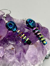 Load image into Gallery viewer, Spooky blue skull beads come with rainbow hematite spine earrings. These stylish skull earrings are perfect for adding a unique flair to any outfit. Whether you&#39;re looking for a Dia De Los Muertos accessory or simply looking to draw inspiration, these goth pieces perfectly capture the vampire goth, witchy, dark, Chingona Cabrona, Latina Chicana styles.   Measurements: 1 1/4” in length
