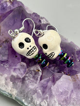 Load image into Gallery viewer, Peruvian off white ceramic skull beads come with rainbow hematite spine earrings. These stylish skull earrings are perfect for adding a unique flair to any outfit. Whether you&#39;re looking for a Dia De Los Muertos accessory or simply looking to draw inspiration, these goth pieces perfectly capture the vampire goth, witchy, dark, Chingona Cabrona, Latina Chicana styles.  Measurements: 1 1/4” in length
