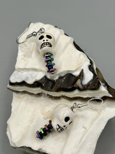 Load image into Gallery viewer, Peruvian off white ceramic skull beads come with rainbow hematite spine earrings. These stylish skull earrings are perfect for adding a unique flair to any outfit. Whether you&#39;re looking for a Dia De Los Muertos accessory or simply looking to draw inspiration, these goth pieces perfectly capture the vampire goth, witchy, dark, Chingona Cabrona, Latina Chicana styles.  Measurements: 1 1/4” in length
