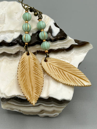 Single-stranded earring features bone carved leaf charm earrings with light mint green melon Czech faceted round glass beads.  Glass beads have a tint of light gold shimmer. Antique antique brass plated steel ear-wire French Hook Earrings.   Measurements: 3” in length  