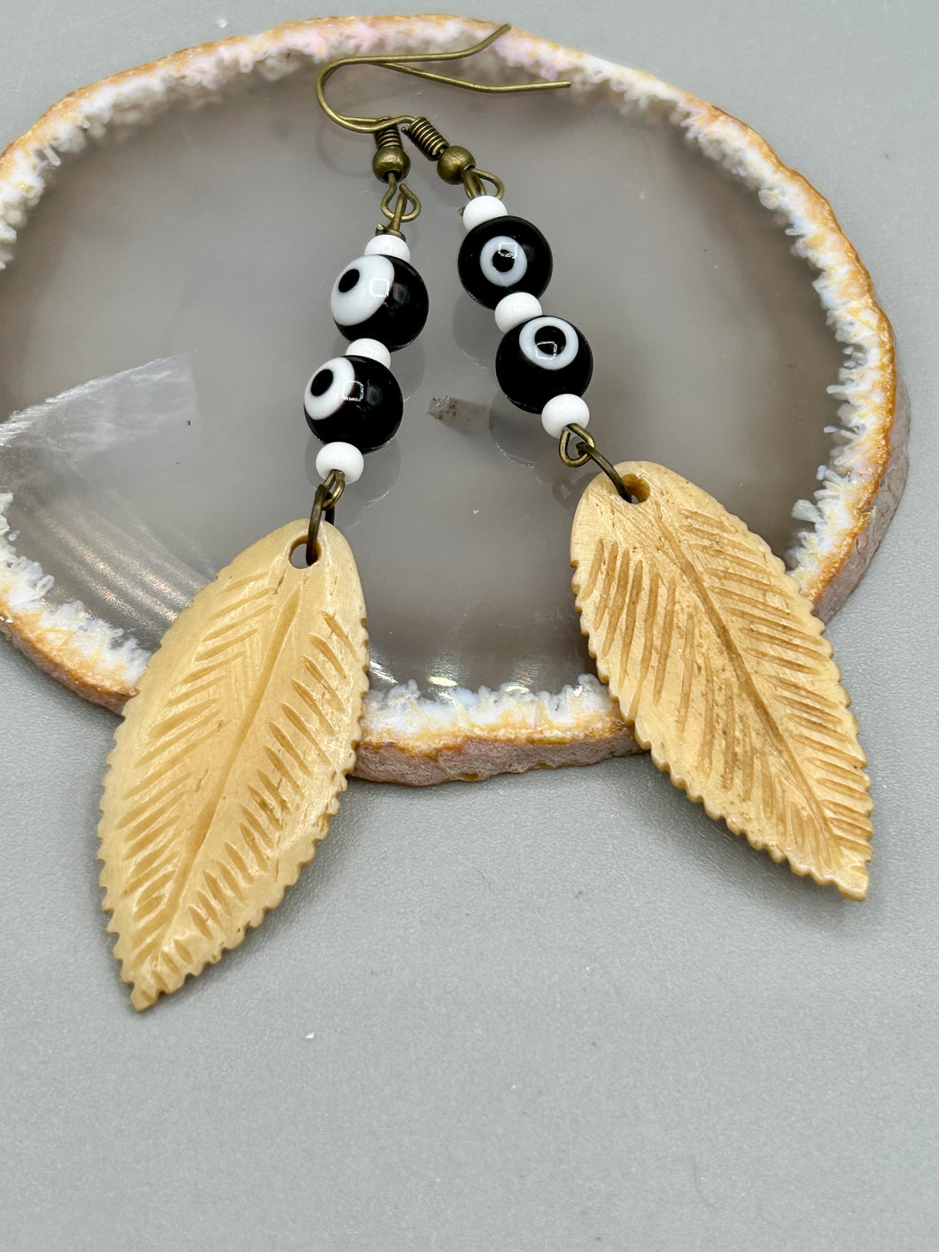 Single-stranded earring features bone carved leaf charm earrings with black and white eye-dot glass beads. Antique Copper Plated Surgical Steel Hammered Long Ear-wire French Hook Earrings.  Measurements: 3” in length  