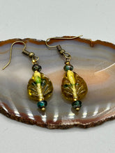 Load image into Gallery viewer, This pair of earrings features a dark amber and green tone, pressed glass leaf charm in an iridescent finish that gives off subtle hues of gold. Complemented with dark teal and gold glass beaded earrings, this set is sure to sparkle.  Measurements: 1 1/4&quot; length
