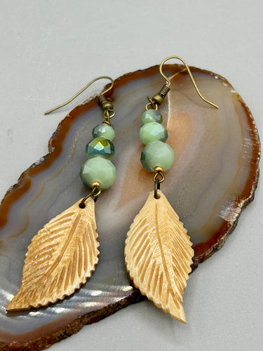 Single-stranded earring features bone carved leaf charm earrings with light mint faceted round glass beads.  Glass beads have a tint of dark green and gold shimmer. Antique antique brass plated steel ear-wire French Hook Earrings.   Measurements: 3” in length  