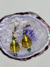 Load image into Gallery viewer, This pair of earrings features a dark amber and green tone, pressed glass leaf charm in an iridescent finish that gives off subtle hues of gold. Complemented with dark teal and gold glass beaded earrings, this set is sure to sparkle.  Measurements: 1 1/4&quot; length

