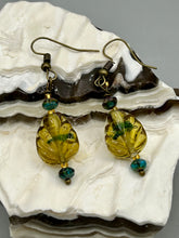 Load image into Gallery viewer, This pair of earrings features a dark amber and green tone, pressed glass leaf charm in an iridescent finish that gives off subtle hues of gold. Complemented with dark teal and gold glass beaded earrings, this set is sure to sparkle.  Measurements: 1 1/4&quot; length
