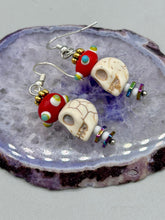 Load image into Gallery viewer, Spooky but festive skull beads with hematite bead spines and come with fiesta shaped crown glass earrings. These stylish skull earrings are perfect for adding a unique flair to any outfit. Whether you&#39;re looking for a Dia De Los Muertos accessory or simply looking to draw inspiration, these goth pieces perfectly capture the vampire goth, witchy, dark, Chingona Cabrona, Latina Chicana styles.   Measurements: 1 1/2” in length
