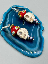 Load image into Gallery viewer, Spooky but festive skull beads with hematite bead spines and come with fiesta shaped crown glass earrings. These stylish skull earrings are perfect for adding a unique flair to any outfit. Whether you&#39;re looking for a Dia De Los Muertos accessory or simply looking to draw inspiration, these goth pieces perfectly capture the vampire goth, witchy, dark, Chingona Cabrona, Latina Chicana styles.   Measurements: 1 1/2” in length

