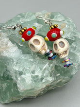 Load image into Gallery viewer, Spooky but festive skull beads with hematite bead spines and come with fiesta shaped crown glass earrings. These stylish skull earrings are perfect for adding a unique flair to any outfit. Whether you&#39;re looking for a Dia De Los Muertos accessory or simply looking to draw inspiration, these goth pieces perfectly capture the vampire goth, witchy, dark, Chingona Cabrona, Latina Chicana styles.   Measurements: 1 1/2” in length
