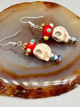 Load image into Gallery viewer, Spooky but festive skull beads with hematite bead spines and come with fiesta shaped crown glass earrings. These stylish skull earrings are perfect for adding a unique flair to any outfit. Whether you&#39;re looking for a Dia De Los Muertos accessory or simply looking to draw inspiration, these goth pieces perfectly capture the vampire goth, witchy, dark, Chingona Cabrona, Latina Chicana styles.   Measurements: 1 1/2” in length
