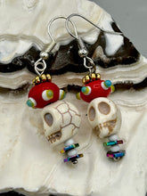 Load image into Gallery viewer, Spooky but festive skull beads with hematite bead spines and come with fiesta shaped crown glass earrings. These stylish skull earrings are perfect for adding a unique flair to any outfit. Whether you&#39;re looking for a Dia De Los Muertos accessory or simply looking to draw inspiration, these goth pieces perfectly capture the vampire goth, witchy, dark, Chingona Cabrona, Latina Chicana styles.   Measurements: 1 1/2” in length
