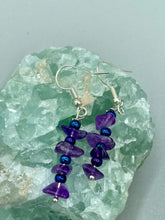 Load image into Gallery viewer, These Lapis Stone Chip Beaded Hoop Earrings feature a dark blue-tone pressed glass leaf charm with an iridescent shimmer finish showcasing hues of gold, purple, blue and pink. The earrings display natural lapis stone chips and royal blue with gold glass beads.  Measurements: 1 1/2&quot; length
