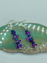 Load image into Gallery viewer, These Lapis Stone Chip Beaded Hoop Earrings feature a dark blue-tone pressed glass leaf charm with an iridescent shimmer finish showcasing hues of gold, purple, blue and pink. The earrings display natural lapis stone chips and royal blue with gold glass beads.  Measurements: 1 1/2&quot; length
