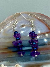 Load image into Gallery viewer, These Lapis Stone Chip Beaded Hoop Earrings feature a dark blue-tone pressed glass leaf charm with an iridescent shimmer finish showcasing hues of gold, purple, blue and pink. The earrings display natural lapis stone chips and royal blue with gold glass beads.  Measurements: 1 1/2&quot; length

