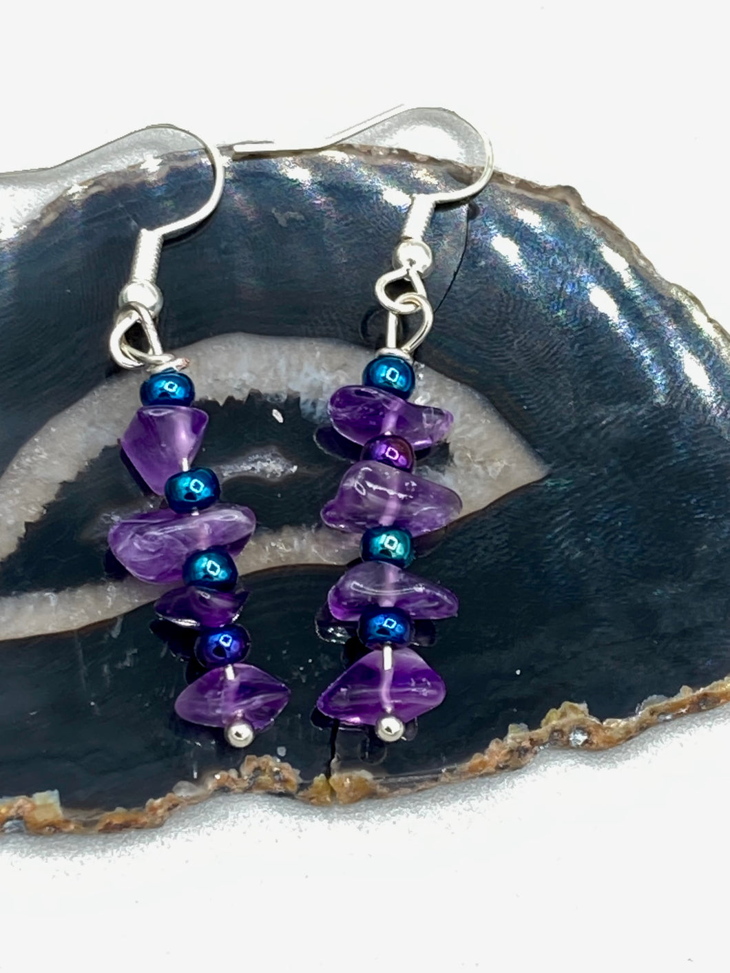 These Lapis Stone Chip Beaded Hoop Earrings feature a dark blue-tone pressed glass leaf charm with an iridescent shimmer finish showcasing hues of gold, purple, blue and pink. The earrings display natural lapis stone chips and royal blue with gold glass beads.  Measurements: 1 1/2