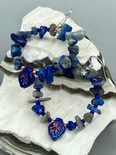 Load image into Gallery viewer, These Lapis Stone Chip Beaded Hoop Earrings feature a dark blue-tone pressed glass leaf charm with an iridescent shimmer finish showcasing hues of gold, purple, blue and pink. The earrings display natural lapis stone chips and royal blue with gold glass beads.  Measurements: 1 1/2&quot; length

