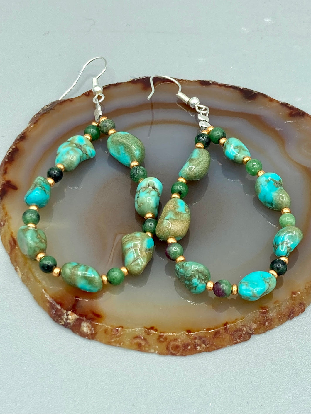 Our Blue-Green Magnesite Stone Beaded Hoop Earrings provide a nature-inspired look that is perfect for any boho-chic style. These earrings feature natural magnesite stone beads with small beads of turquoise and gold glass for subtle accent. Show off your bohemian look with these eye-catching hoops.  Measurements: 2 1/2