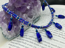 Load image into Gallery viewer, This Vibrant Royal Blue Glass Beaded Choker Necklace features two adjustable strands of deep blue beads with purple hues. The Bohemian style jewelry includes a mixture of rectangular-shaped blue, purple, and silver glass beads, which come together to create an eye-catching and elegant look. Perfect for any outfit, this draping necklace will add a vibrant and bold touch to your style.  Measurements:    Necklace is 14 3/4” in length, can be adjusted up to 16"
