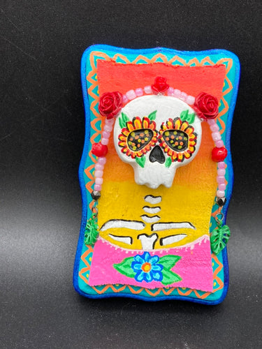 Transform your walls with this handcrafted polymer clay wall art. Showcasing a vibrant Frida Kahlo inspired calavera with hand-beaded floral crown, this Day of the Dead wall decor piece is perfect for adding a traditional Mexican folk art touch to any home.