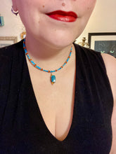 Load image into Gallery viewer, This adjustable choker style necklace features an eye-catching teal wood scarab beetle pendant and glass beaded strands. This dramatic necklace is kept together by double-hole flat matte lava-red beads, providing a collar shape. The necklace artfully wraps around the neck, conveying an elegant and bold style.  Measurements:    Necklace is 14 1/2” in length, can be adjusted up to 16&quot; 
