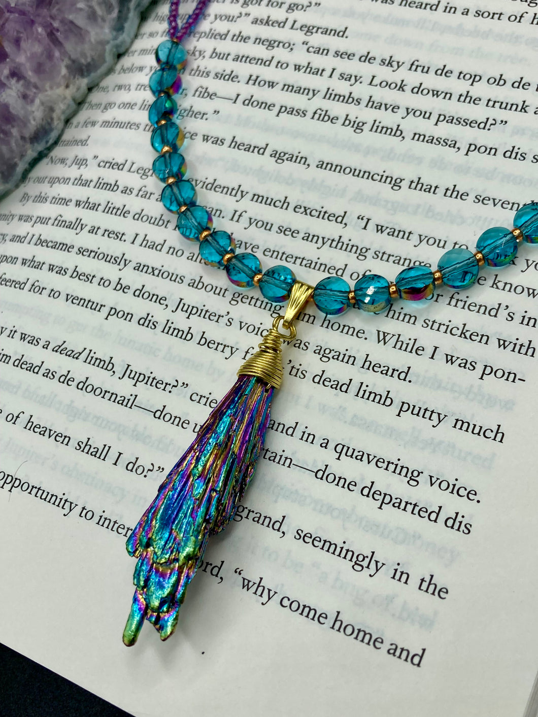 This necklace boasts a stunning Rainbow Kyanite wired stone pendant and two strands of shimmering glass beads. The blues contain hues of pink, gold, blue and green, offering a vibrant and bold addition to any jewelry collection.  Measurements:  Necklace is 17” in length, can be adjusted to 18