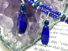 Load image into Gallery viewer, This Vibrant Royal Blue Glass Beaded Choker Necklace features two adjustable strands of deep blue beads with purple hues. The Bohemian style jewelry includes a mixture of rectangular-shaped blue, purple, and silver glass beads, which come together to create an eye-catching and elegant look. Perfect for any outfit, this draping necklace will add a vibrant and bold touch to your style.  Measurements:    Necklace is 14 3/4” in length, can be adjusted up to 16"

