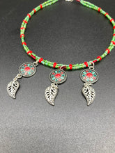 Load image into Gallery viewer, This adjustable necklace features an eye-catching Southwest-inspired design. Multi-hued glass beads, including bright green and vibrant red, are accompanied by dark red and green pendants with silver-plated feather charms. Ideal for chingona guerrera carbonas, la India princesses, warrior cosplay, and native-inspired looks.  Measurements:  Necklace is 15” adjustable up to 17" in length
