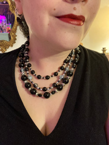 This stunning Shimmery black glass and floral metal beaded necklace features three long strands which gracefully drape around the neck. Its bold elegance is the perfect accessory for a cocktail chic outfit, a wedding, or a more minimalist look.  Measurements:    Necklace is 16 1/4” in length - adjustable to 18