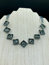 Load image into Gallery viewer, This two-strand necklace, crafted from aqua-blue and silver toned glass beads, is a stunning statement piece. The addition of faceted triangle-shaped glass beads tucked between hematite square beads adds an exquisite and unique flair. The necklace gracefully drapes around the neck, bringing an air of bold and elegant flair to any ensemble it complements. 15” in length, can be extended up to 17"
