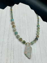 Load image into Gallery viewer, This exquisite necklace showcases earthy tones of mossy green ceramic beads, complemented by a gray toned howlite stone chip pendant. To add a sparkle, I interspersed gold-tone glass beads between each ceramic one. Two delicate strands feature small glass beads with hues of blue, gold, and purple. These are bridged by flower-shaped gold plated beads, which then unite with the round ceramic beads. This alluring earth-tone combination makes a stunning accessory. Necklace is 17” 
