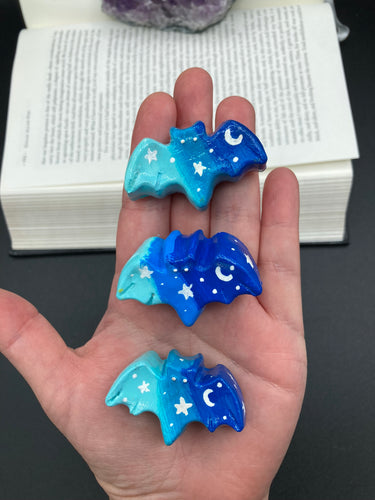 Cute and spooky magnet design to adorn your refrigerator, lockers, workstation, toolbox, or dishwasher. This hand-sculpted clay bat statuette boasts stunning ombre coloration, transitioning from dark blue to light blue to recreate the breathtaking look of a starry night sky.  H 1” x W 2” x D 1/2”