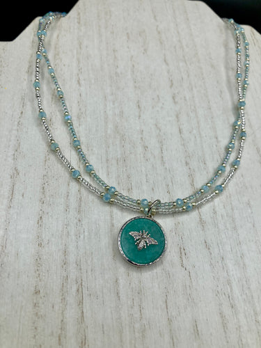 Make a statement with this dainty, yet bold Amazonite Bee Pendant Necklace. Beautifully beaded with frosty glass in blue and silver tones, this shabby chic jewelry piece complements any outfit. The perfect combination of hues and shapes will add complexity and elegance to your look.  Measurements:    Necklace is 17” in length