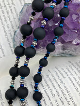 Load image into Gallery viewer, This statement piece features 3 long strands of flat matte black and dark blue glass beads, complemented by a floral metal beaded necklace. It gracefully drapes across the neck for a fierce, yet elegant look, making it perfect for cocktail chic attire, weddings, or minimalist styling.  Measurements:    Necklace is 16” in length - adjustable to 18&quot;
