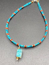 Load image into Gallery viewer, This adjustable choker style necklace features an eye-catching teal wood scarab beetle pendant and glass beaded strands. This dramatic necklace is kept together by double-hole flat matte lava-red beads, providing a collar shape. The necklace artfully wraps around the neck, conveying an elegant and bold style.  Measurements:    Necklace is 14 1/2” in length, can be adjusted up to 16&quot; 
