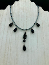 Load image into Gallery viewer, This adjustable collar-style necklace features silver and black glass beads in a combination of both teardrop and rectangular shapes, designed to create visual complexity and depth. The two strands are held together with two-hole silver and black beads, creating a stunningly bold and elegant draped collar that enhances any outfit.
