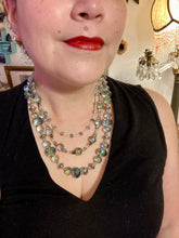 Load image into Gallery viewer, This beautiful necklace features shimmery, rich aqua blue and silver tones glass beads. Its three strands consist primarily of faceted rondelle shaped beads, along with a variety of lighter blue and silver beads, resulting in a unique multicolored look. The perfect statement piece, this elegant necklace will drape beautifully across your neck, adding a vibrant hue to any Spring outfit.  Measurements:    Necklace is 18” in length
