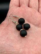 Load image into Gallery viewer, These flat matte black glass bead earrings are perfect for creating a cocktail chic ensemble. With a round shape and silver plated floral bead, this timeless piece is ideal for special occasions such as weddings. Its minimalist look exudes effortless elegance. Measurements: 1 1/4” in length
