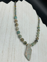Load image into Gallery viewer, This exquisite necklace showcases earthy tones of mossy green ceramic beads, complemented by a gray toned howlite stone chip pendant. To add a sparkle, I interspersed gold-tone glass beads between each ceramic one. Two delicate strands feature small glass beads with hues of blue, gold, and purple. These are bridged by flower-shaped gold plated beads, which then unite with the round ceramic beads. This alluring earth-tone combination makes a stunning accessory. Necklace is 17” 
