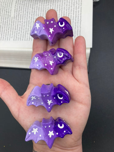 Cute and spooky magnet design to adorn your refrigerator, lockers, workstation, toolbox, or dishwasher. This hand-sculpted clay bat statuette boasts stunning ombre coloration, transitioning from dark purple to light purple to recreate the breathtaking look of a starry night sky.  H 1” x W 2” x D 1/2”