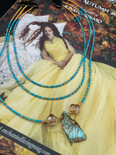 Load image into Gallery viewer, This vibrant and enchanting Southwestern Style inspired necklace is comprised of three strands. The first two feature a mix of blue and green turquoise and gold glass beads, while the longest strand features a howlite stone chip dyed turquoise and shimmery cross faceted champaign color glass beads for a dramatic look.  Measurements: The Necklace is 16” and can be adjusted up to 18" 
