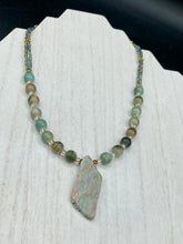 Load image into Gallery viewer, This exquisite necklace showcases earthy tones of mossy green ceramic beads, complemented by a gray toned howlite stone chip pendant. To add a sparkle, I interspersed gold-tone glass beads between each ceramic one. Two delicate strands feature small glass beads with hues of blue, gold, and purple. These are bridged by flower-shaped gold plated beads, which then unite with the round ceramic beads. This alluring earth-tone combination makes a stunning accessory. Necklace is 17” 
