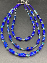 Load image into Gallery viewer, This vibrant royal blue and silver-tone necklace is adjustable and features an eye-catching three-strand design. The rectangular blue glass beads are predominant, complemented by a blend of lighter blue and silver beads for an intriguing multi-hued finish. By mixing shapes and tones, it creates a complex, dimensional look. The draped effect adds a fierce yet elegant pizzazz to any outfit. Perfect for the season of Spring, it will bring a splash of rich color to your wardrobe. 
