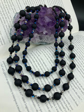 Load image into Gallery viewer, This statement piece features 3 long strands of flat matte black and dark blue glass beads, complemented by a floral metal beaded necklace. It gracefully drapes across the neck for a fierce, yet elegant look, making it perfect for cocktail chic attire, weddings, or minimalist styling.  Measurements:    Necklace is 16” in length - adjustable to 18&quot;
