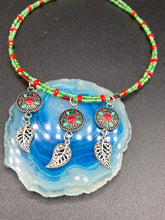 Load image into Gallery viewer, This adjustable necklace features an eye-catching Southwest-inspired design. Multi-hued glass beads, including bright green and vibrant red, are accompanied by dark red and green pendants with silver-plated feather charms. Ideal for chingona guerrera carbonas, la India princesses, warrior cosplay, and native-inspired looks.  Measurements:  Necklace is 15” adjustable up to 17" in length
