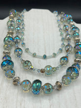 Load image into Gallery viewer, This beautiful necklace features shimmery, rich aqua blue and silver tones glass beads. Its three strands consist primarily of faceted rondelle shaped beads, along with a variety of lighter blue and silver beads, resulting in a unique multicolored look. The perfect statement piece, this elegant necklace will drape beautifully across your neck, adding a vibrant hue to any Spring outfit.  Measurements:    Necklace is 18” in length
